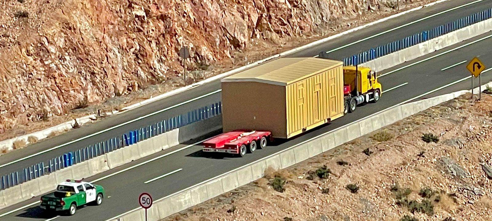 Vista aérea de un convoy de Logística Inversol trasladando un módulo sobredimensionado por una carretera de montaña, con una patrulla de Carabineros escoltando por la pista contraria